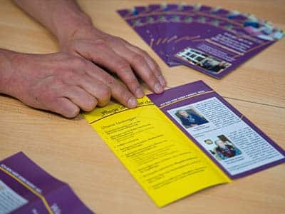 lila Flyer auf dem Tisch Hände die etwas auf einem Flyer des Heide-Pflegedienstes zeigen zu Schulungszwecken und Beratung